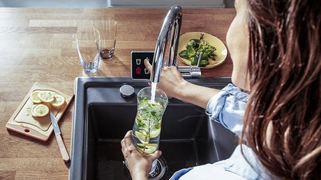 Eine Frau die ein Glas unter einer Kuechenspuele fuellt