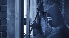 Ein Einbrecher der ein Fenster mit einer Brechstange öffnet