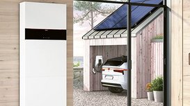 Ein Flur mit einem Stromspeicher mit einem blick nach draußen, dort sieht man ein Garagendach mit einer Photovoltaikanlage und eine Wallbox und ein Elektro Auto